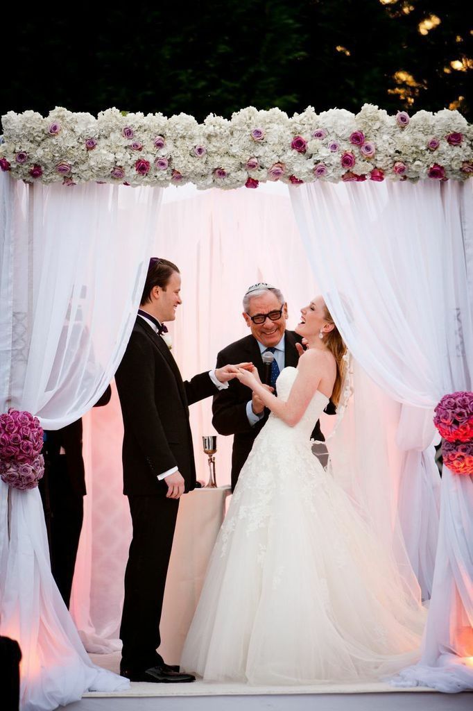 Vows and joyful laughter under white Chuppah with hydrangeas and roses. Photo by Fred Marcus.