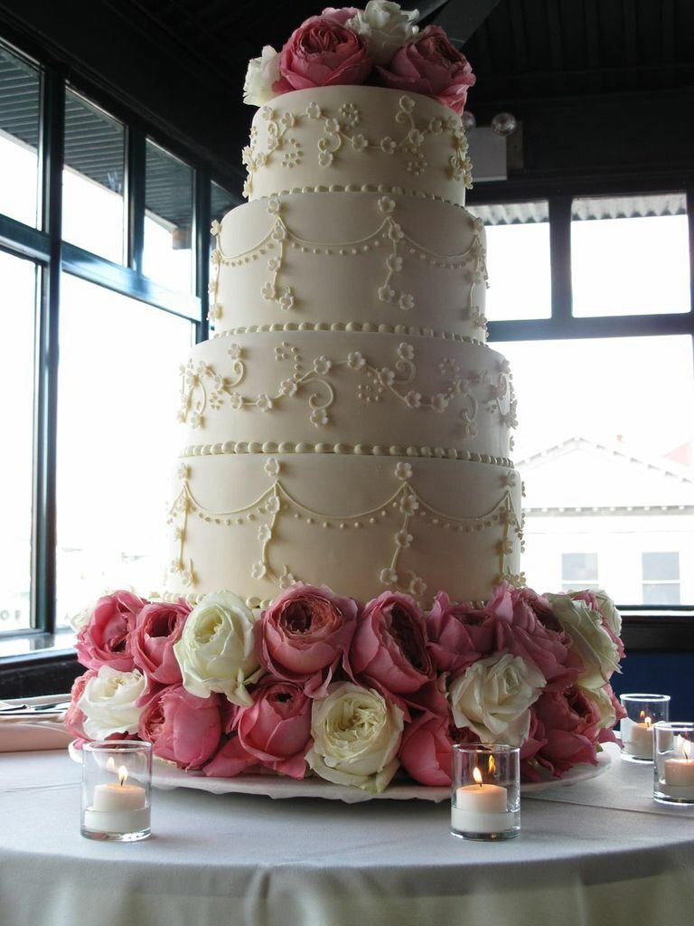 Deep pink and cream garden roses on a tired wedding cake with floral piping.